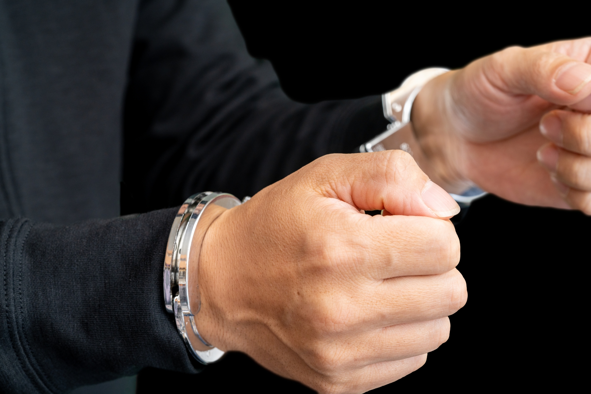 手錠をかけられた人物のシルエット。違法行為が刑事罰につながるリスクを象徴。